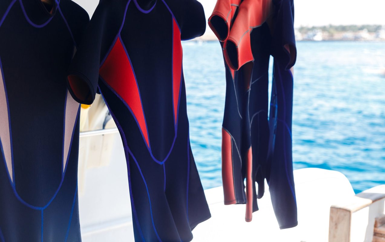4 short wetsuits hanging with sea in background